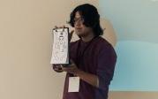 A student holds up a design on a whiteboard.